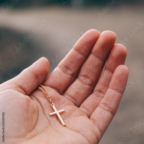 Eine Hand die ein goldenes Kreuz behutsam hält. Symbolisiert Vertrauen in Gott, Glaube, Kruzifix, Religion und Christentum.