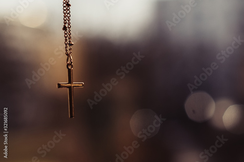 goldenes kruzifix das an einer Halskette hängt und vor einem stimmungsvollen warmen Bokeh baumelt