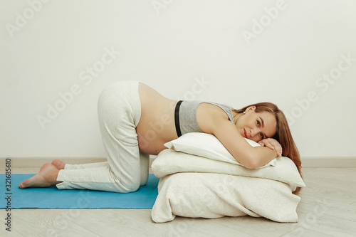 Young pregnant mom is engaged in exercises before childbirth. Beautiful girl with a big belly kneeling in the room.