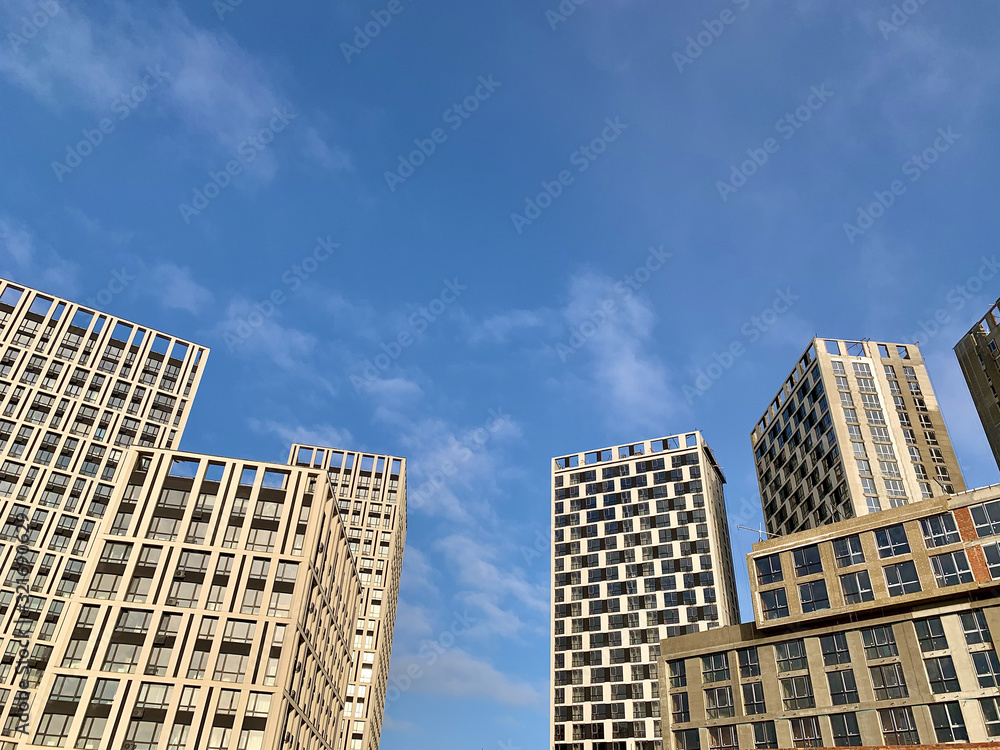 Fototapeta premium High-rise building on a background of blue sky. Tall new building with mirrored windows, bottom view. Background texture: office building.
