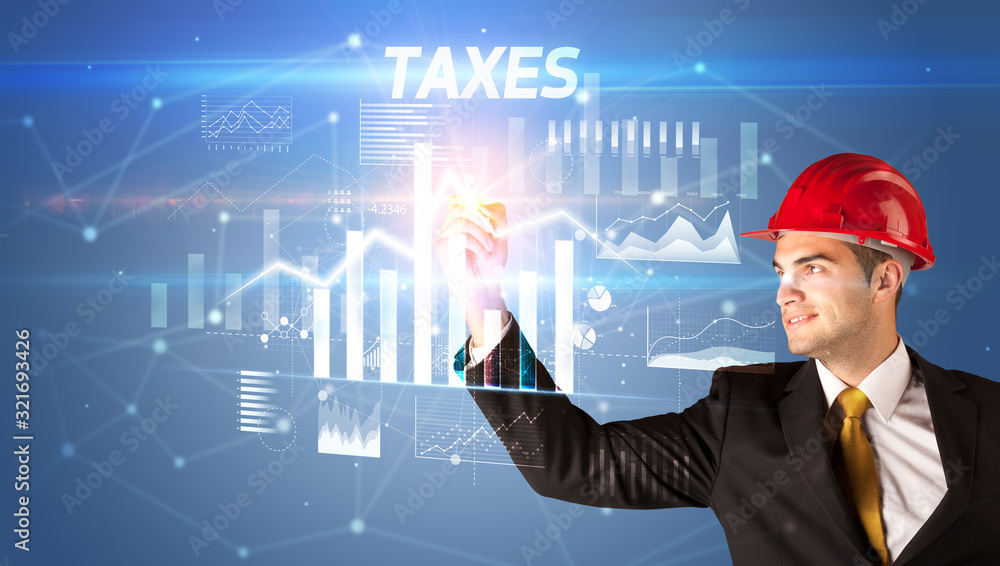 Handsome businessman with helmet drawing TAXES inscription, architecture business plan concept Handsome businessman with helmet drawing TAXES inscription, architecture business plan concept