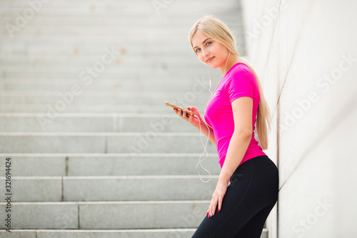 beautiful young woman in sportswear in the summer on the street in headphones with a phone in her hands