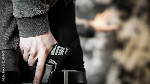 Man holding out hand while drawing a concealed pistol. Personal protection concept photo