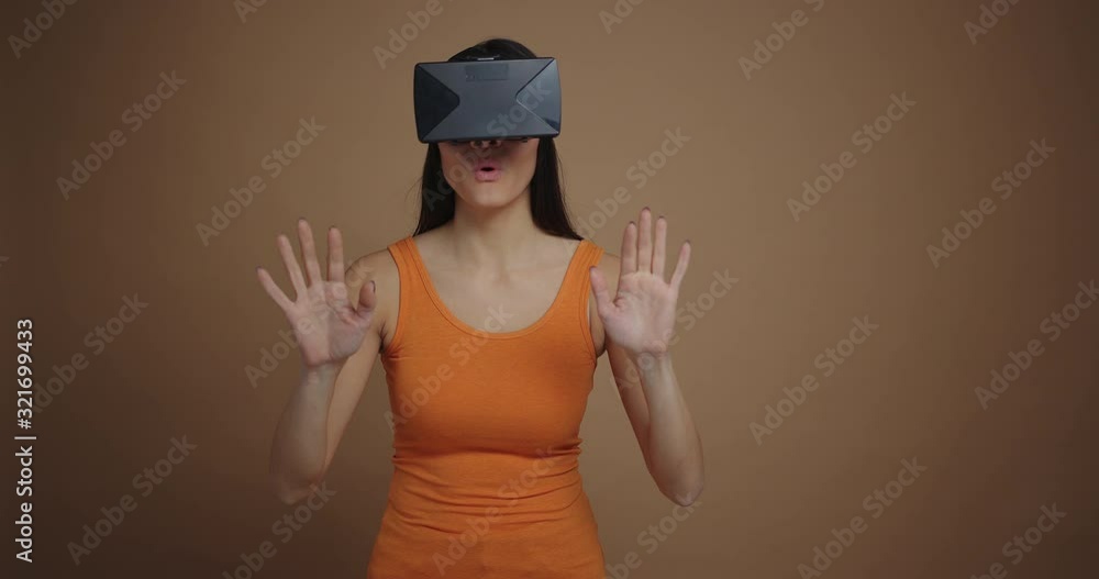 Amazed smiling woman wearing virtual reality glasses isolated on brown background Amazed smiling woman wearing virtual reality glasses isolated on brown background