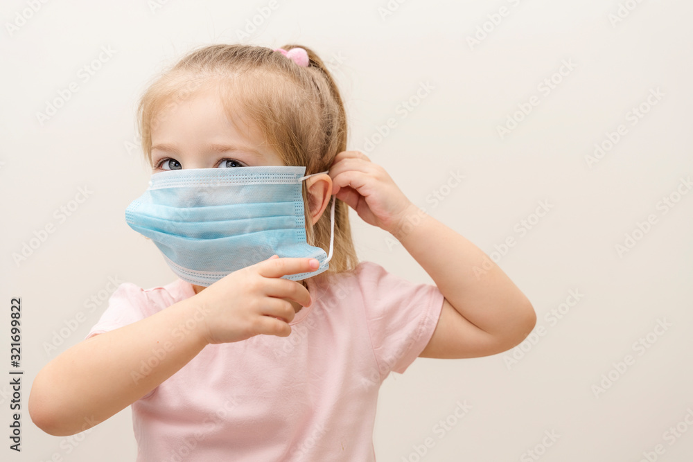 little girl puts on a disposable mask on a light background. Chinese virus epidemic protection