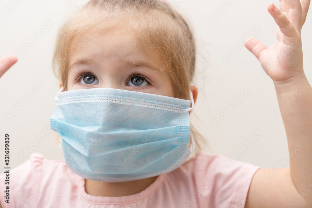 little girl in a disposable mask on a light background. fear is on his face, hands are raised up. Chinese virus, pandemic protection