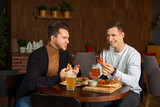 Two happy male friends laughing and talking over a glass of beer at the local pub. Young men relaxing, drinking delicious craft beer together at the bar. Communication, lifestyle, weekend concept