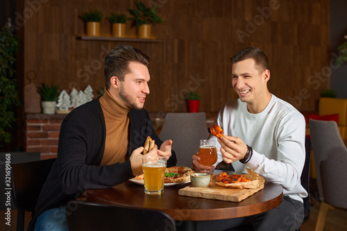 Two happy male friends laughing and talking over a glass of beer at the local pub. Young men relaxing  drinking delicious craft beer together at the bar. Communication  lifestyle  weekend concept