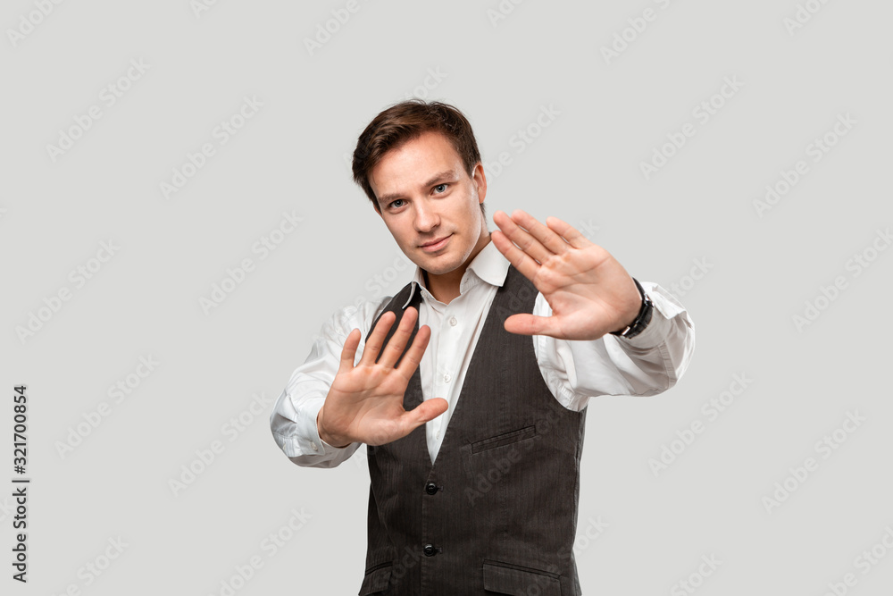 Confindent handsome man in a white shirt and grey vest expressing Stop gesture Confindent handsome man in a white shirt and grey vest expressing Stop gesture