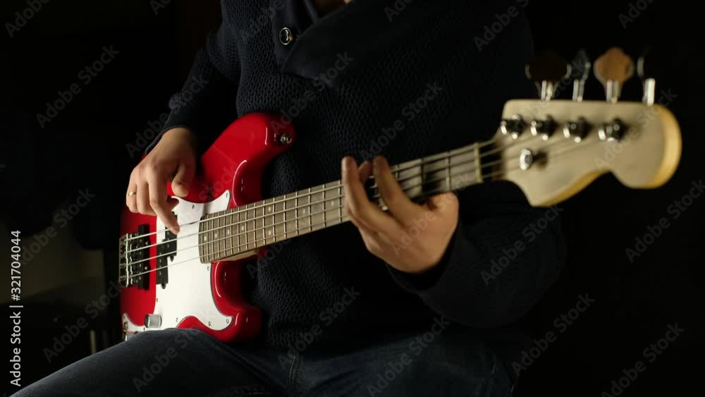 man plays electric bass guitar. Black background. The color of the guitar is red. overall plan. man plays electric bass guitar. Black background. The color of the guitar is red. overall plan.