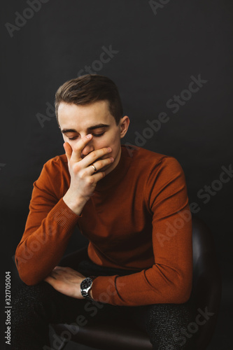 Desperate, sad, worried or upset young man with his eyes closed holding his head. black background.