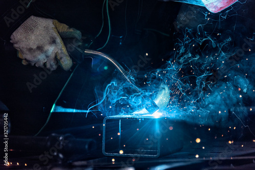 Close up of MIG welding torch on metal with sparks and fumes illuminated by the blue light of the high temperature flame