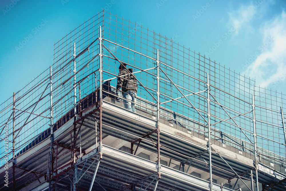 Naklejka premium metallic safety net in construction industry, man working on scaffolding (unidentified person)