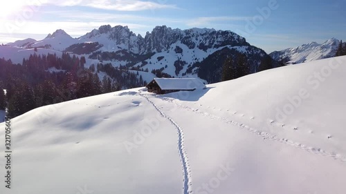 passage by drone on a breathtaking landscape in the sun in the Swiss alps with an uninhabited chalet in the high snow and a typical pointed mountain range in the background