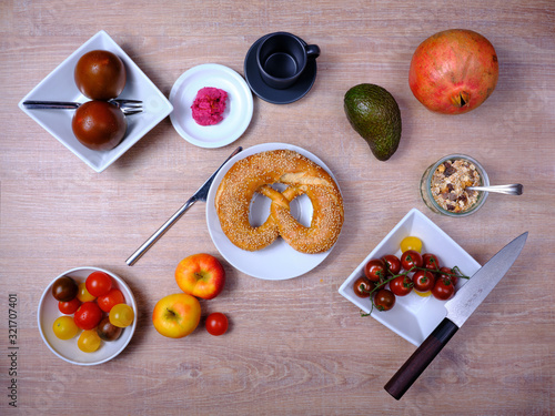 Pretzel, sweet tea-cake, marmelade, avocado, tomatoes, a pomegranate and a glass of orange juice, symetrically arranged on a wooden table on white and black tableware photo