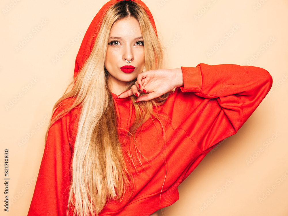 Portrait of young beautiful hipster bad girl in trendy red summer hoodie and earring in her nose.Sexy carefree smiling blond woman posing in studio.Positive model having fun Portrait of young beautiful hipster bad girl in trendy red summer hoodie and earring in her nose.Sexy carefree smiling blond woman posing in studio.Positive model having fun