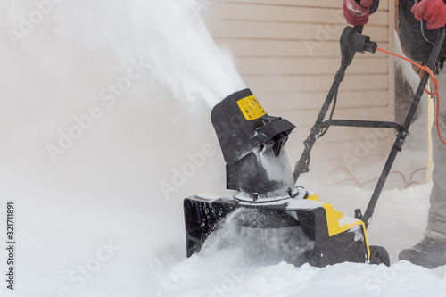 Man is brushing white snow with the yellow electric snow thrower in a winter garden © Tatiana Kuklina