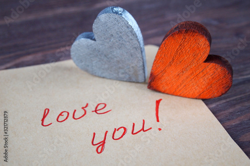 Foto Two wooden hearts and a note with the words love you on a wooden background