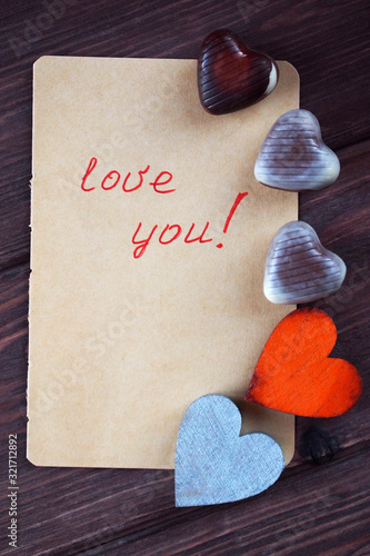 Bild auf Leinwand Two wooden hearts, chocolates and a note with the words love you on a wooden background