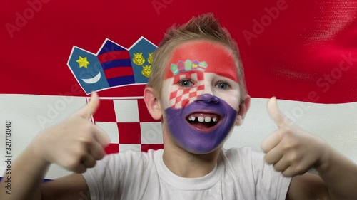 Joyful fan on the background of the flag of Croatia. Happy boy with painted face in national colors. The young fan rejoices in the victory of his beloved team. Success. Victory. Triumph. photo