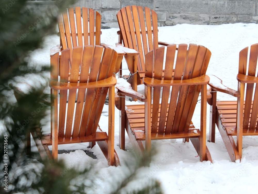 Warm orange wood Adirondack chairs installed in the street of Old Montreal in winter for sitting and eating out in the heart of the city in a group.