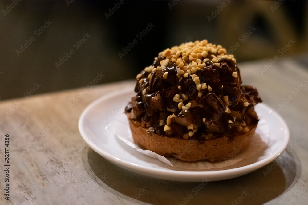 Chocolate muffin cake with nuts and choco cream on white plate on wooden table. Dessert chocolate baked treat