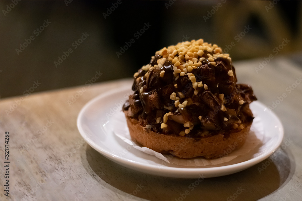 Chocolate muffin cake with nuts and choco cream on white plate on wooden table. Dessert chocolate baked treat Chocolate muffin cake with nuts and choco cream on white plate on wooden table. Dessert chocolate baked treat