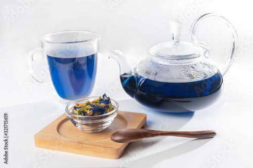 filled teapot and glass cup of blue tea near wooden spoon and bowl filled blue thai tea