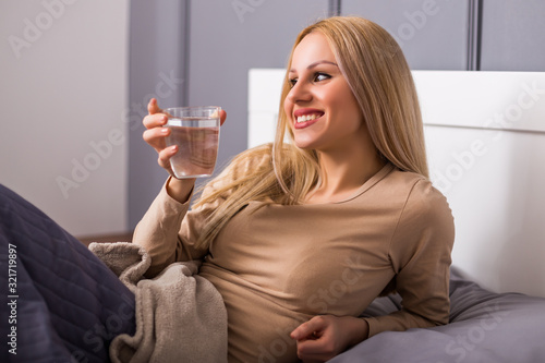 Beautiful woman drinking water and sitting on bed.	