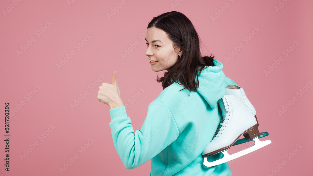 Figure skating, Hobbies and a healthy active lifestyle. A cheerful girl in a bright hoodie with skates on her shoulder Figure skating, Hobbies and a healthy active lifestyle. A cheerful girl in a bright hoodie with skates on her shoulder