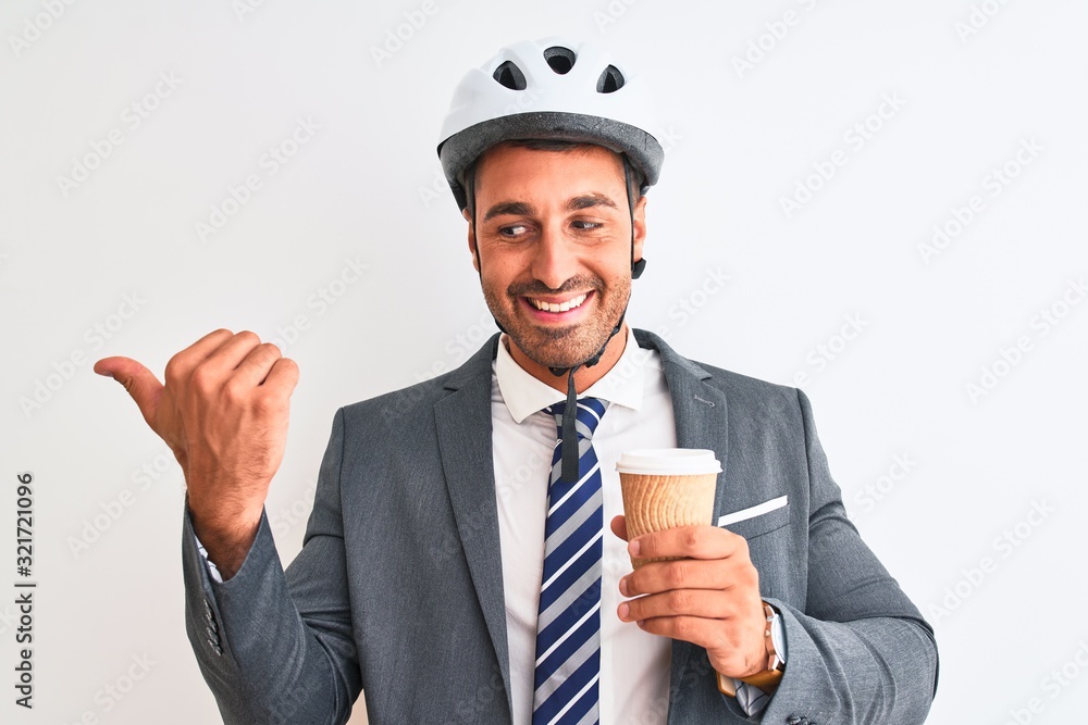 Young handsome business man wearing bike helmet and take away coffee over isolated background pointing and showing with thumb up to the side with happy face smiling Young handsome business man wearing bike helmet and take away coffee over isolated background pointing and showing with thumb up to the side with happy face smiling