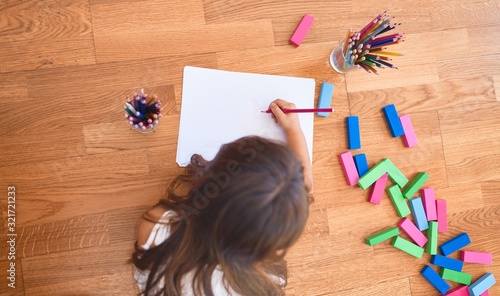 Adorable toddler lying down on the floor drawing using paper and pencils at kindergarten