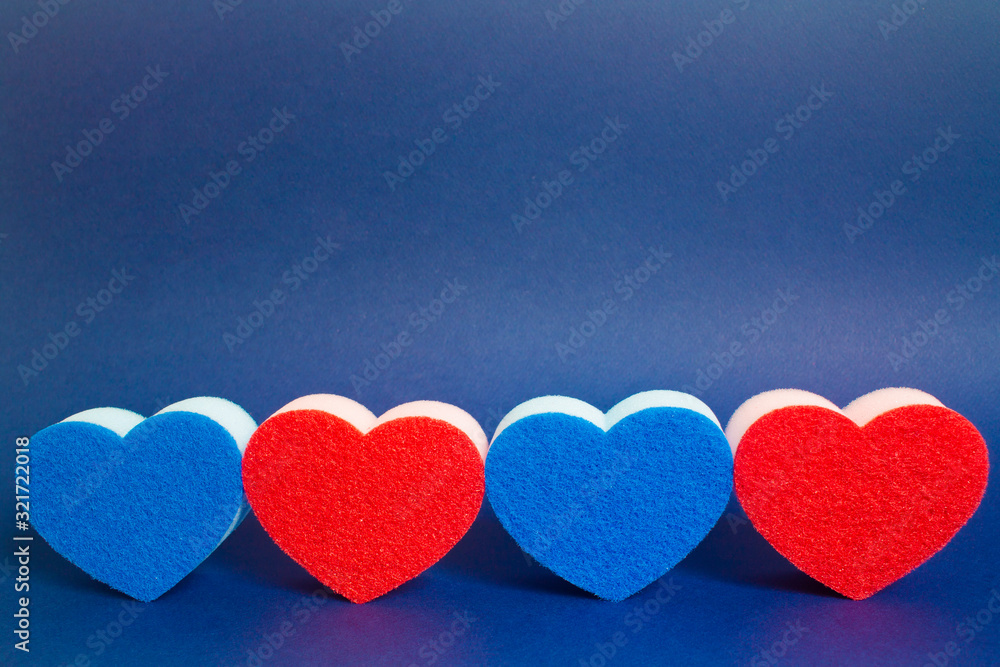 Obraz premium Four red and blue heart shape dishwasher sponge in the foreground on the blue background