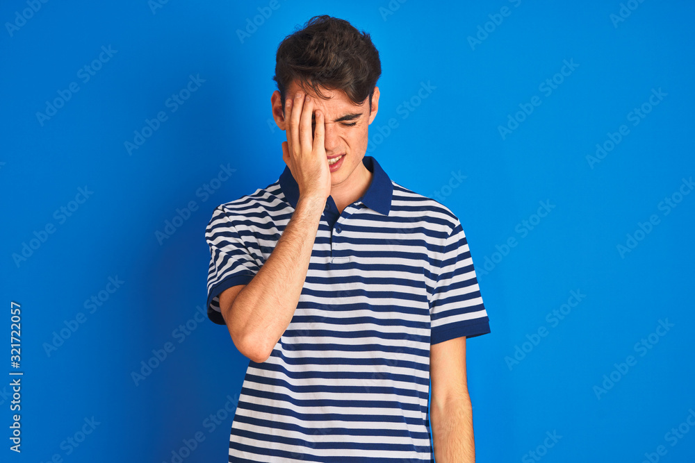 Teenager boy wearing casual t-shirt standing over blue isolated background Yawning tired covering half face, eye and mouth with hand. Face hurts in pain.
