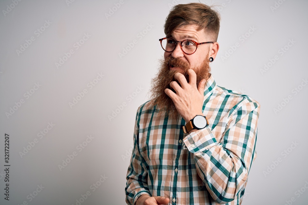 Handsome Irish redhead man with beard wearing glasses and hipster shirt with hand on chin thinking about question, pensive expression. Smiling with thoughtful face. Doubt concept. Handsome Irish redhead man with beard wearing glasses and hipster shirt with hand on chin thinking about question, pensive expression. Smiling with thoughtful face. Doubt concept.