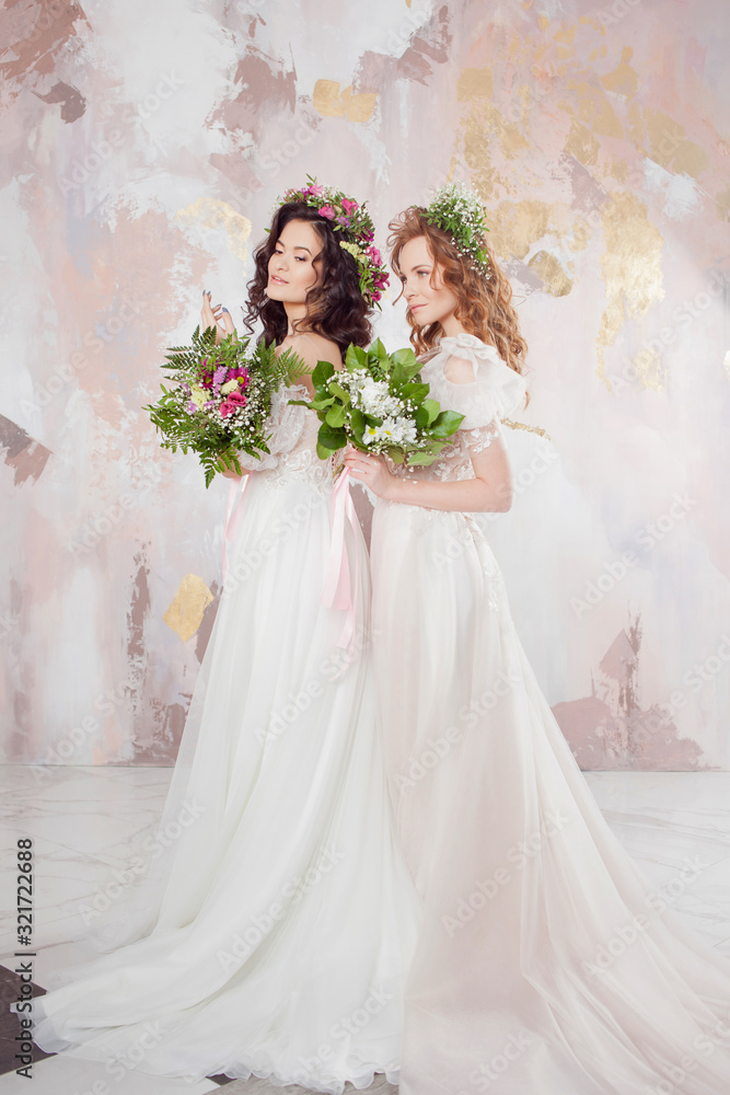 Two charming brides in beautiful spring wreaths on their heads. Beautiful young women in wedding dresses Two charming brides in beautiful spring wreaths on their heads. Beautiful young women in wedding dresses