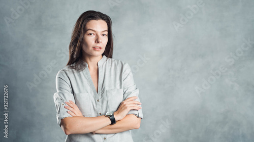 Young successful confident woman in a gray shirt against a textured gray wall.