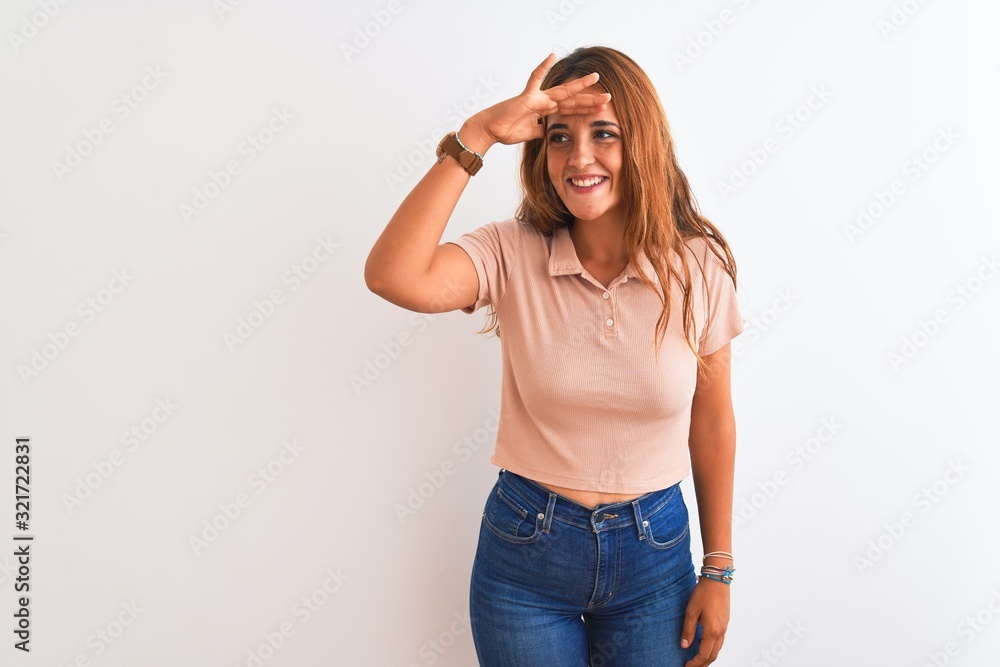 Young redhead woman stading over white isolated background very happy and smiling looking far away with hand over head. Searching concept. Young redhead woman stading over white isolated background very happy and smiling looking far away with hand over head. Searching concept.