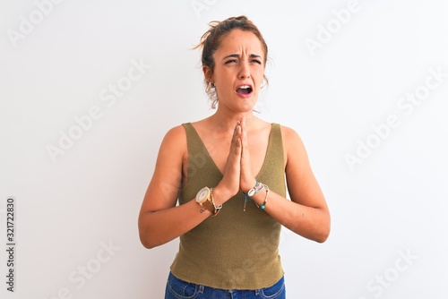 Young redhead woman wearing a bun over isolated background begging and praying with hands together with hope expression on face very emotional and worried. Asking for forgiveness. Religion concept. © Krakenimages.com