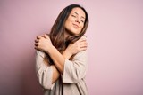 Young beautiful brunette woman wearing casual sweater standing over pink background Hugging oneself happy and positive, smiling confident. Self love and self care