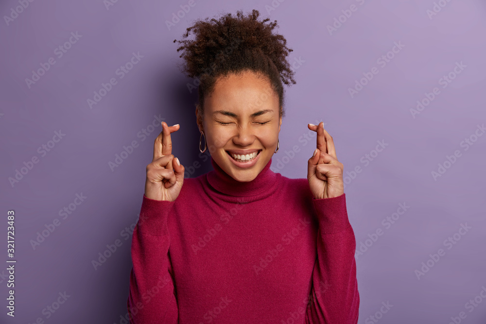 Glad dark skinned model crosses fingers, believes in good luck, smiles broadly with closed eyes, wants dreams come true, wears burgundy turtleneck, awaits for miracle happen, eager receive something Glad dark skinned model crosses fingers, believes in good luck, smiles broadly with closed eyes, wants dreams come true, wears burgundy turtleneck, awaits for miracle happen, eager receive something
