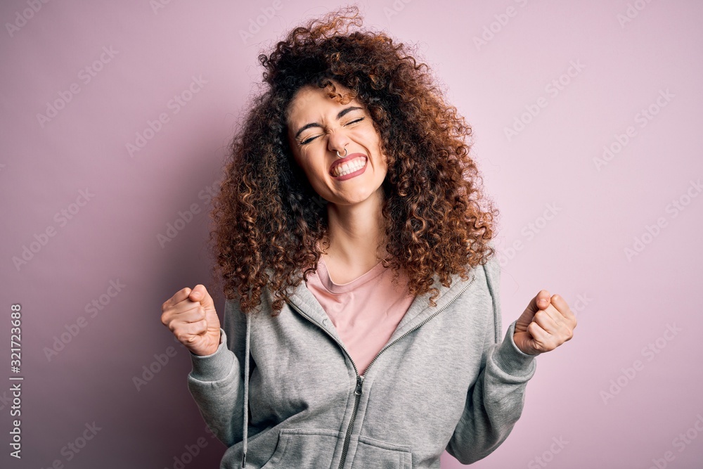 Young beautiful brunette sportswoman with curly hair and piercing wearing sportswear very happy and excited doing winner gesture with arms raised, smiling and screaming for success. Celebration Young beautiful brunette sportswoman with curly hair and piercing wearing sportswear very happy and excited doing winner gesture with arms raised, smiling and screaming for success. Celebration