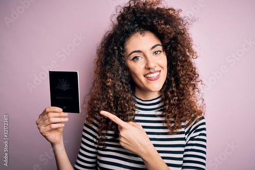Beautiful tourist woman with curly hair and piercing holding australia australian passport id very happy pointing with hand and finger