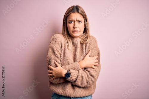 Young beautiful blonde woman wearing winter wool sweater over pink isolated background shaking and freezing for winter cold with sad and shock expression on face