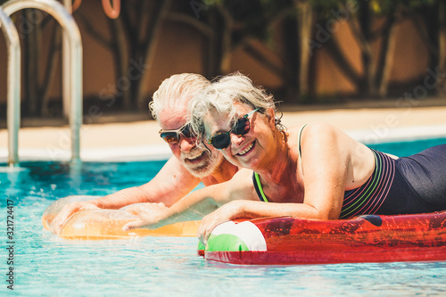 Cheerful happy coule of retired senior old people smile and enjoy together the pool in summer hoiday vacation with coloure trendy lilos in the water - concept of no limit age to have fun and love photo