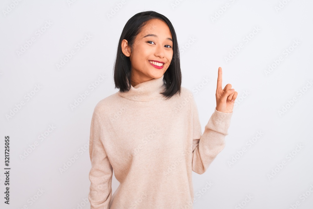 Young chinese woman wearing turtleneck sweater standing over isolated white background showing and pointing up with finger number one while smiling confident and happy. Young chinese woman wearing turtleneck sweater standing over isolated white background showing and pointing up with finger number one while smiling confident and happy.