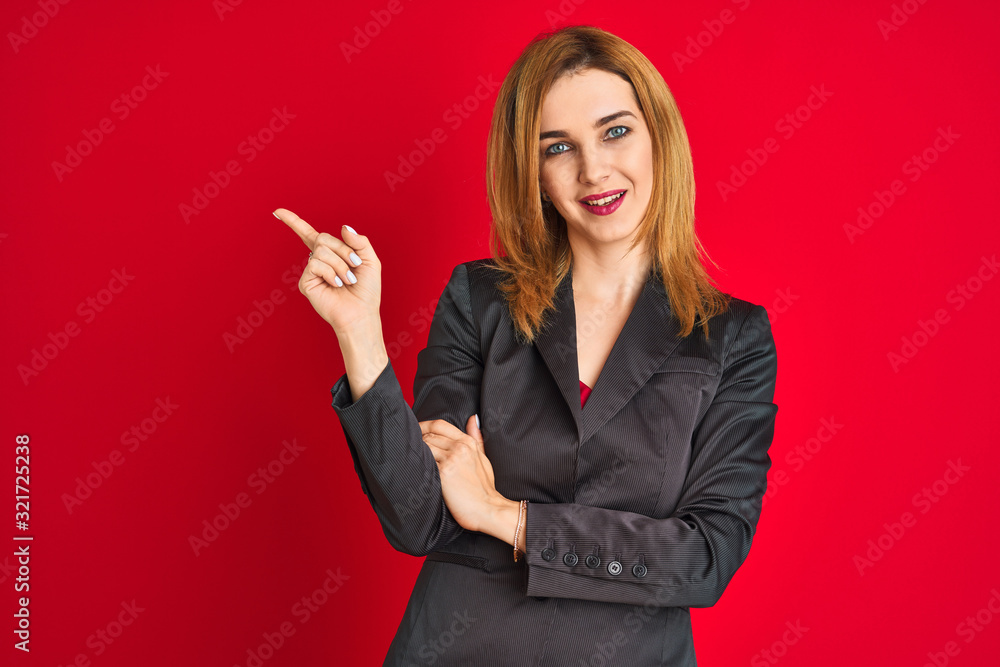 Young caucasian business woman wearing a suit over isolated red background with a big smile on face, pointing with hand and finger to the side looking at the camera.