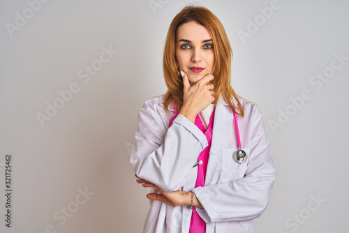 Redhead caucasian doctor woman wearing pink stethoscope over isolated background looking confident at the camera with smile with crossed arms and hand raised on chin. Thinking positive.