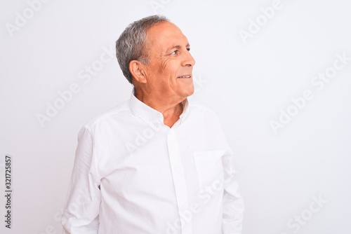 Senior grey-haired man wearing elegant shirt standing over isolated white background looking away to side with smile on face, natural expression. Laughing confident.
