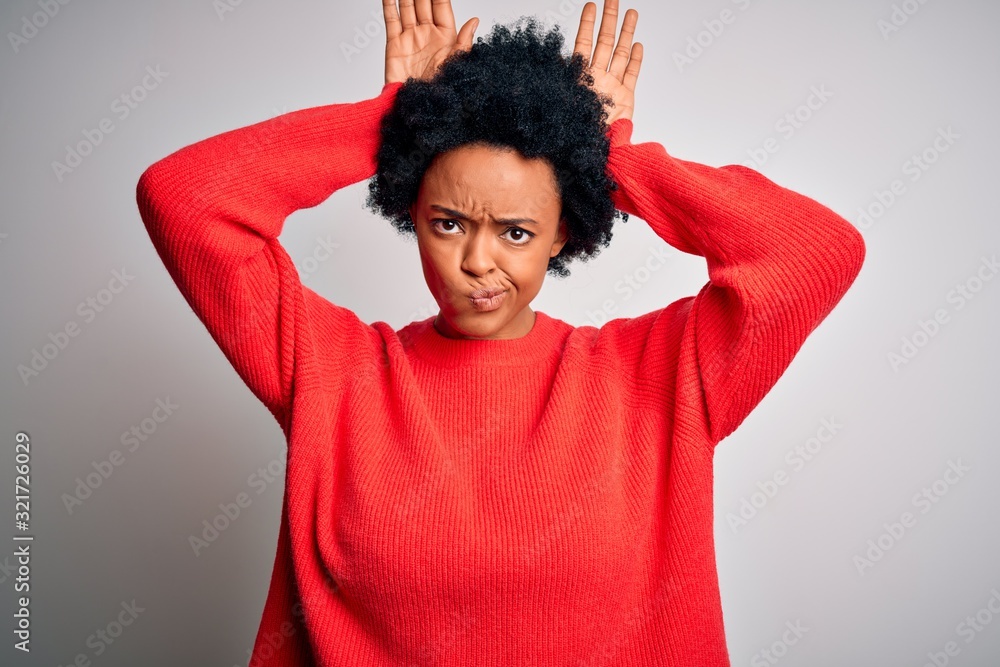 Young beautiful African American afro woman with curly hair wearing red casual sweater Doing bunny ears gesture with hands palms looking cynical and skeptical. Easter rabbit concept. Young beautiful African American afro woman with curly hair wearing red casual sweater Doing bunny ears gesture with hands palms looking cynical and skeptical. Easter rabbit concept.